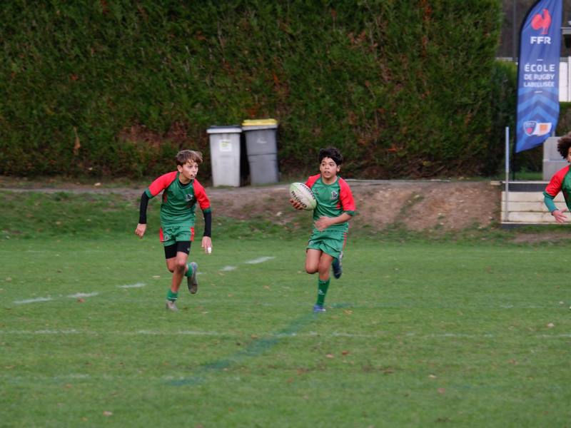 Deux joueurs U14 courent balle en main devant le fanion École de rugby labellisée FFR.