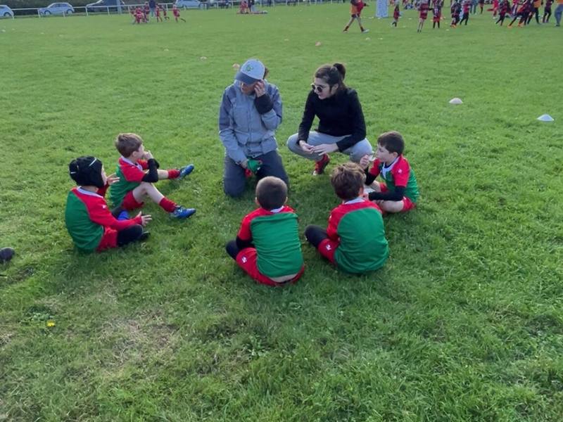 Les U8 assis en cercle sur l'herbe avec leurs éducateurs, pendant un temps d'échange.
